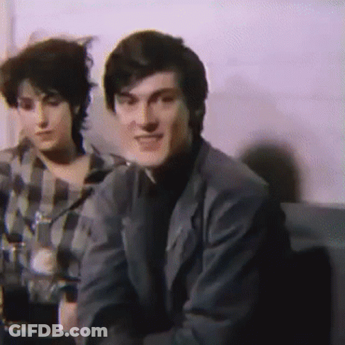 Man In Suit Next To Woman In Plaid Shirt On Couch GIF