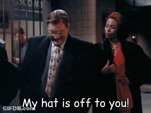 Man In Suit Next To Woman In Red Dress Saying My Hat Is Off To You GIF