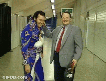 Man In Suit Next To Wrestler In Blue Outfit GIF