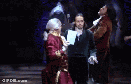Man In Suit On Stage In Front Of Men In Costume GIF