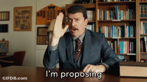 Man In Suit Proposing In Front Of Bookshelf GIF
