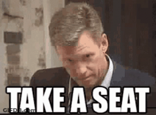 Man In Suit Saying Take A Seat GIF