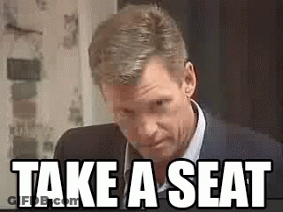 Man In Suit Saying Take A Seat GIF