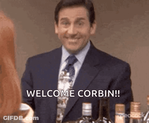 Man In Suit Saying Welcome Corbin Next To Woman GIF