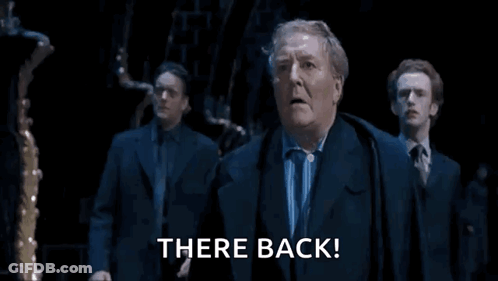 Man In Suit Says There Back In Dark Room GIF