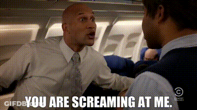 Man In Suit Screaming At Another Man On Airplane GIF