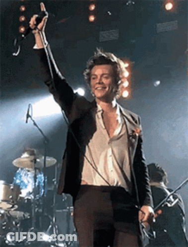 Man In Suit Singing Into Microphone On Stage With Drum Set GIF
