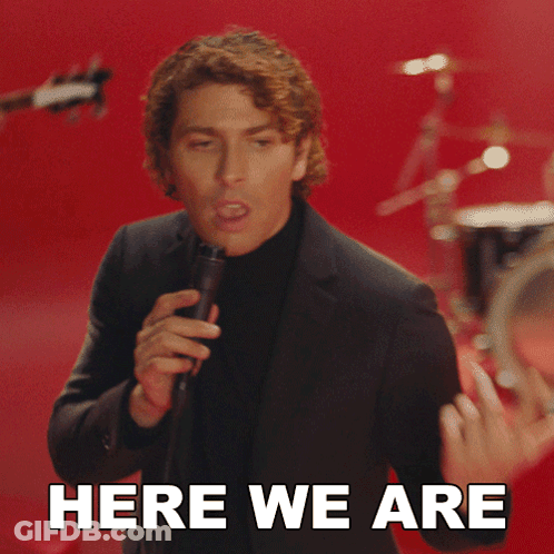 Man In Suit Singing Into Microphone Saying Here We Are GIF