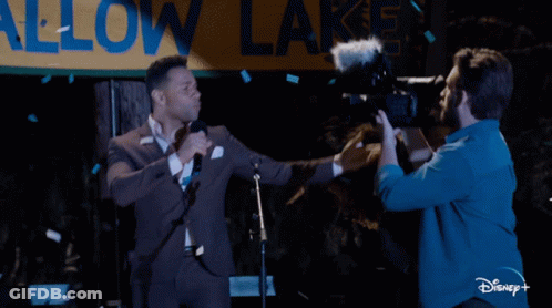 Man In Suit Singing Into Microphone While Cameraman Takes Picture GIF
