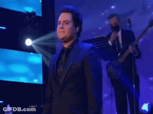 Man In Suit Singing Onstage With Guitarist GIF