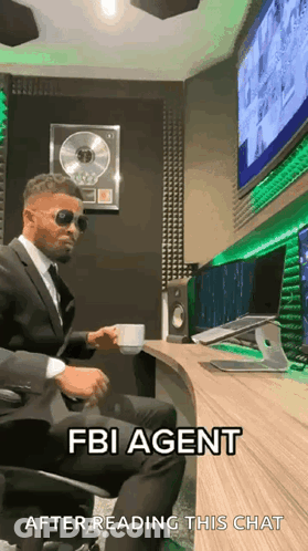 Man In Suit Sitting At Desk With Coffee And Sunglasses GIF