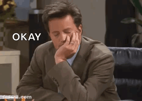 Man In Suit Sitting At Desk With Hand On Chin Saying Okay GIF