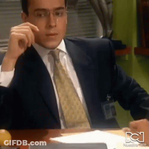 Man In Suit Sitting At Desk With Nuestra Tele Logo GIF