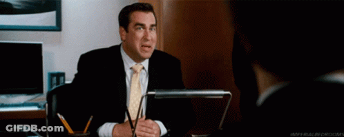 Man In Suit Sitting At Desk With Pow Behind Him GIF