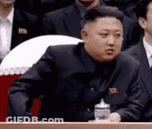 Man In Suit Sitting At Podium In Front Of Crowd GIF