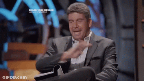 Man In Suit Sitting At Shark Tank Sign GIF