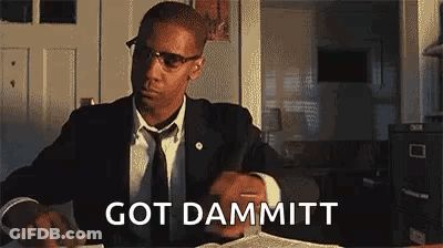 Man In Suit Sitting At Table With Book And Glasses GIF