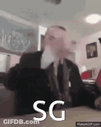 Man In Suit Sitting At Table With SG On Screen GIF