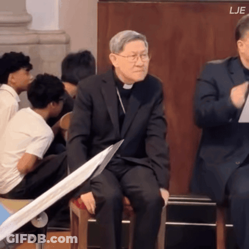Man In Suit Sitting Before Group With LJE Above GIF