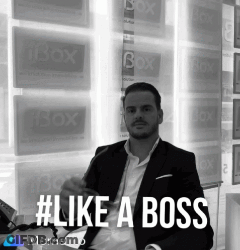Man In Suit Sitting Before Ibox Signs GIF