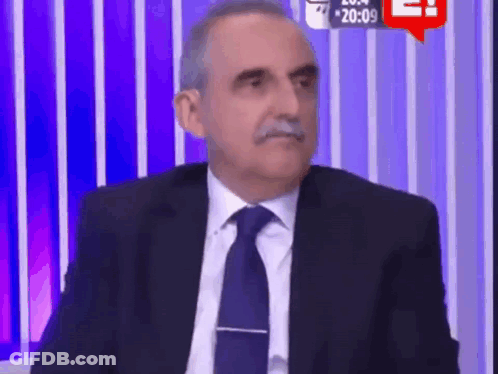 Man In Suit Sitting Before Purple Striped Wall GIF
