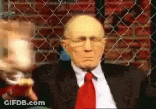 Man In Suit Sitting In Front Of Chain Link Fence GIF