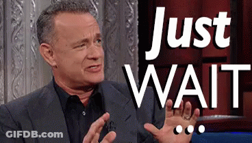 Man In Suit Sitting In Front Of Just Wait Sign GIF