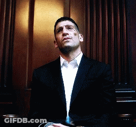 Man In Suit Sitting In Front Of Wooden Wall GIF