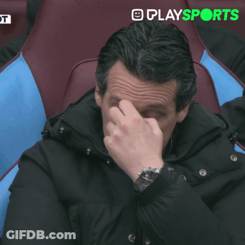 Man In Suit Sitting In Stadium In Front Of Play Sports Screen GIF