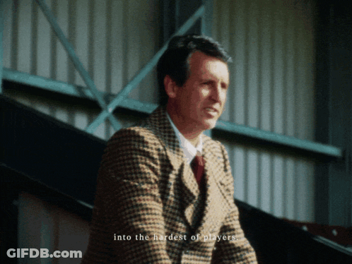 Man In Suit Sitting In Stadium In Front Of Play Sports Screen GIF