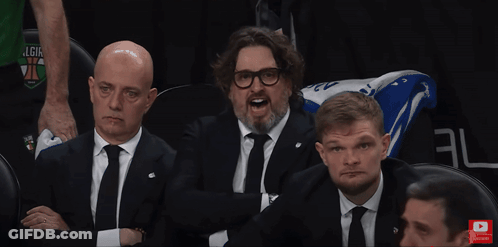 Man In Suit Sitting In Stadium With Arms Up And Subscribe Button GIF