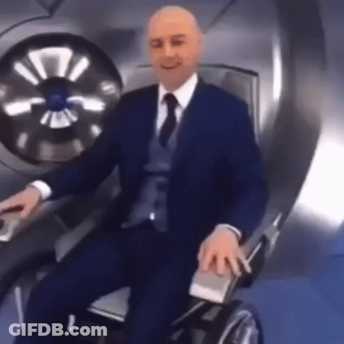Man In Suit Sitting In Wheelchair Holding Remote GIF
