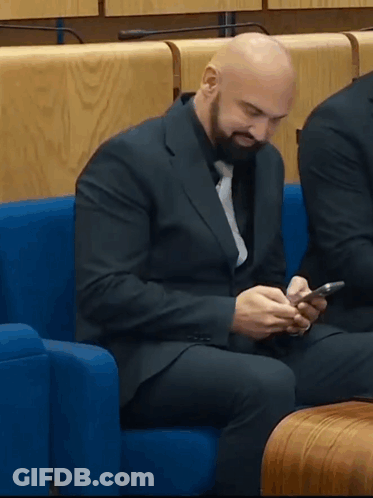 Man In Suit Sitting On Blue Couch Looking At Phone GIF