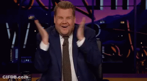 Man In Suit Sitting On Stage With Hands In Air GIF