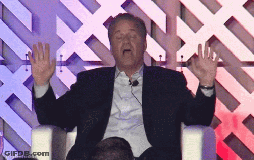 Man In Suit Sitting With Hands Up Saying Big GIF