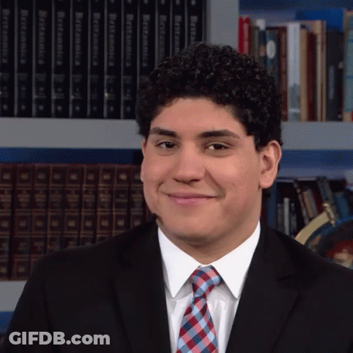 Man In Suit Smiling Before Bookshelf With Dictionary GIF
