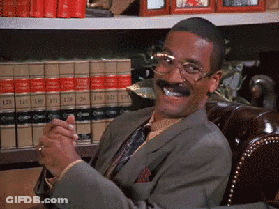Man In Suit Smiling In Front Of Bookshelf GIF