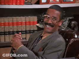 Man In Suit Smiling In Front Of Bookshelf GIF