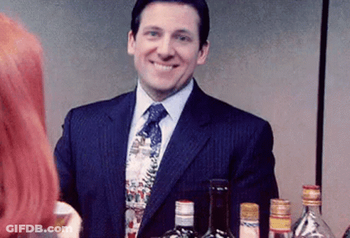 Man In Suit Smiling In Front Of Liquor Bottles GIF