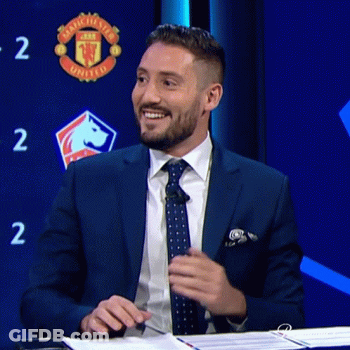 Man In Suit Smiling In Front Of Manchester United Sign GIF