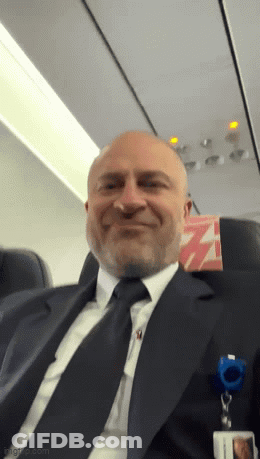 Man In Suit Smiling On Airplane GIF