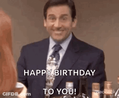 Man In Suit Smiling Saying Happy Birthday To You Next To Woman GIF