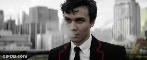 Man In Suit Smoking Cigarette In Front Of City GIF