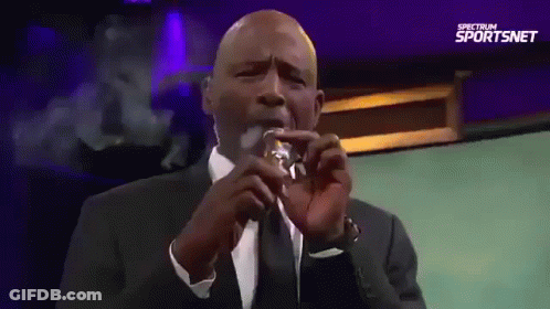 Man In Suit Smoking Cigarette In Front Of Spectrum Sportsnet Sign GIF