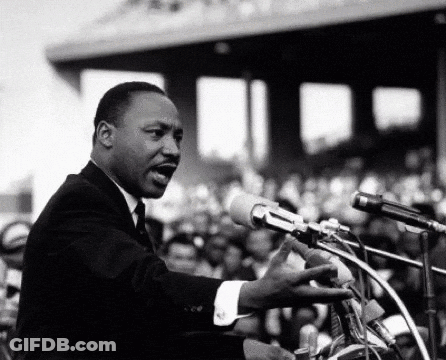 Man In Suit Speaking Into Microphone Before Crowd GIF