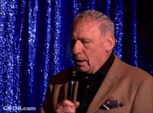 Man In Suit Speaking Into Microphone Blue Curtain GIF