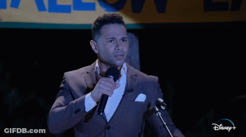 Man In Suit Speaking Into Microphone In Front Of Disney+ Sign GIF