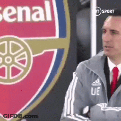 Man In Suit Standing Before Arsenal Logo GIF
