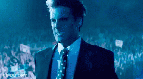 Man In Suit Standing Before Crowd In Dark Room GIF