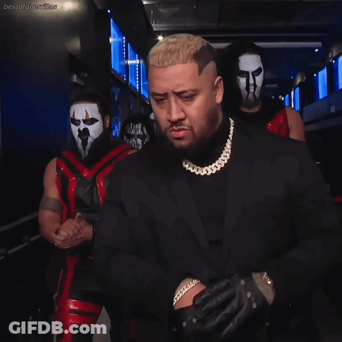 Man In Suit Standing Before Masked Wrestlers GIF